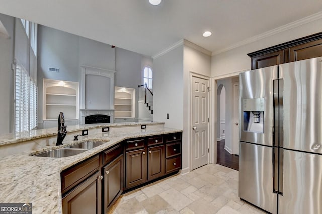 kitchen featuring light stone countertops, stainless steel refrigerator with ice dispenser, ornamental molding, dark brown cabinets, and sink