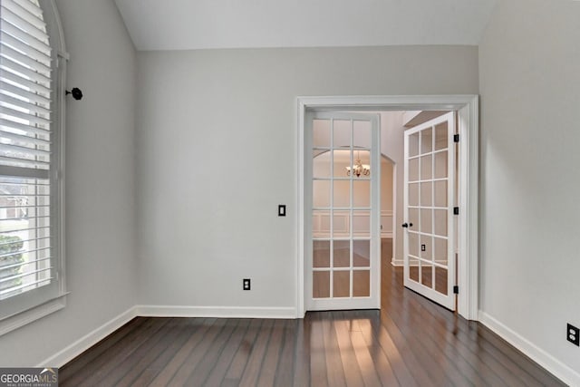 spare room with dark hardwood / wood-style flooring, french doors, and an inviting chandelier