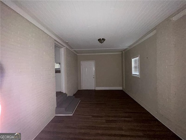 hall with crown molding, dark wood-type flooring, and brick wall