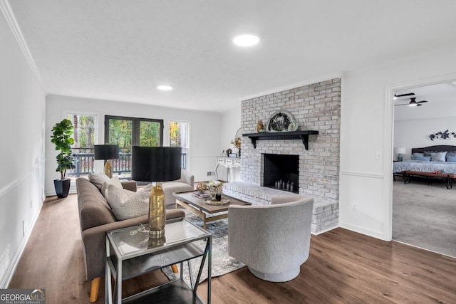 living room with ceiling fan, crown molding, wood-type flooring, and a brick fireplace