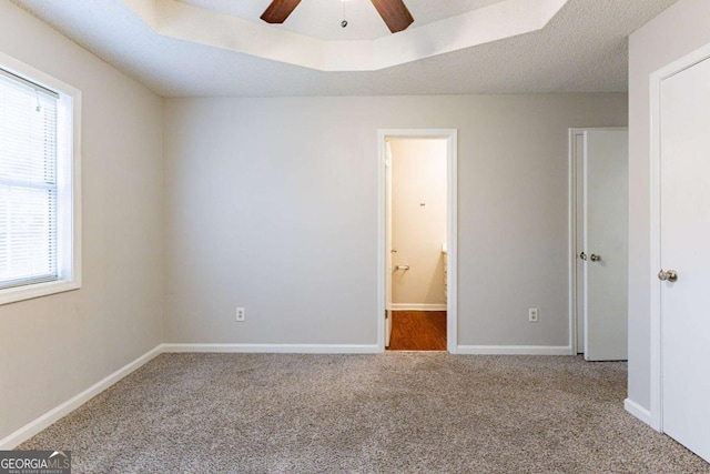 unfurnished bedroom with carpet flooring, a textured ceiling, a tray ceiling, ceiling fan, and connected bathroom