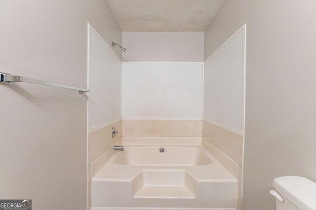 bathroom featuring a bath, a textured ceiling, and toilet