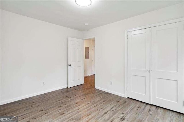 unfurnished bedroom featuring light wood-type flooring, electric panel, and a closet