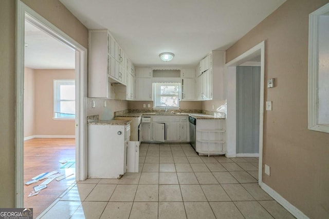 kitchen featuring light tile patterned floors, stainless steel dishwasher, white cabinetry, and a healthy amount of sunlight