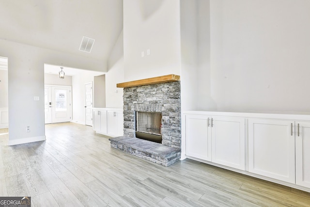 unfurnished living room featuring a stone fireplace, high vaulted ceiling, ceiling fan with notable chandelier, and light wood-type flooring