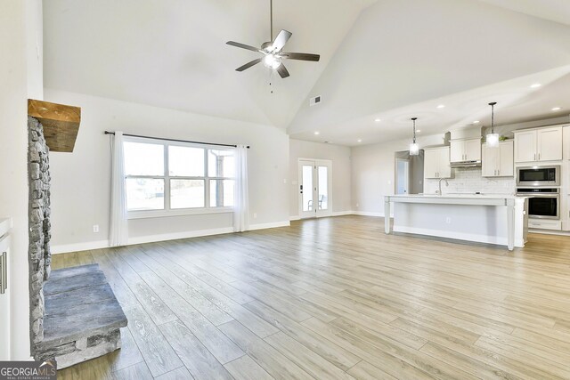 unfurnished living room with high vaulted ceiling, ceiling fan with notable chandelier, and light wood-type flooring