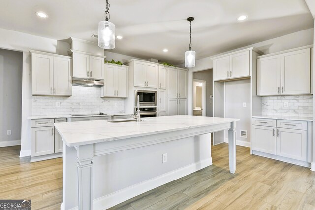 kitchen with decorative light fixtures, stainless steel appliances, a center island with sink, and light hardwood / wood-style floors