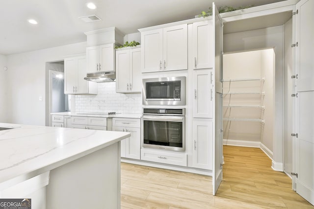 kitchen with light stone counters, backsplash, appliances with stainless steel finishes, white cabinets, and light wood-type flooring