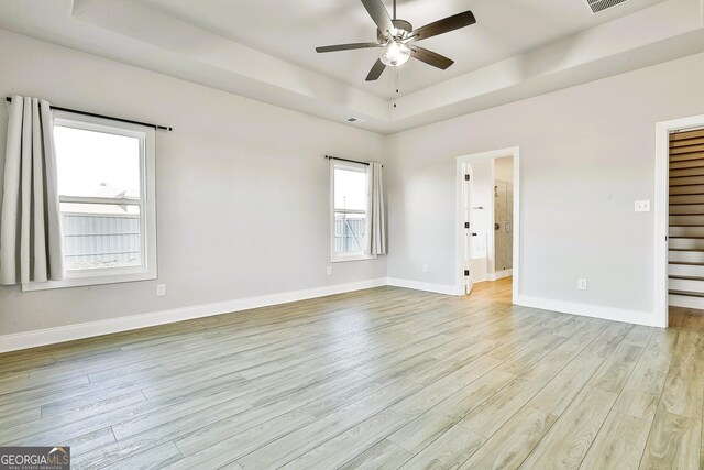 spare room with a tray ceiling, ceiling fan, and light hardwood / wood-style floors