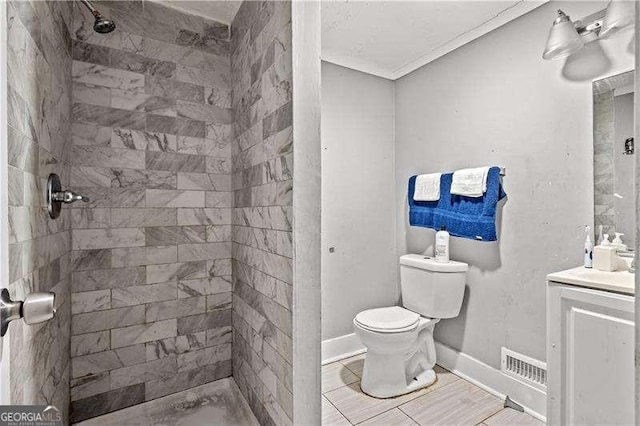 bathroom with vanity, toilet, a tile shower, and crown molding