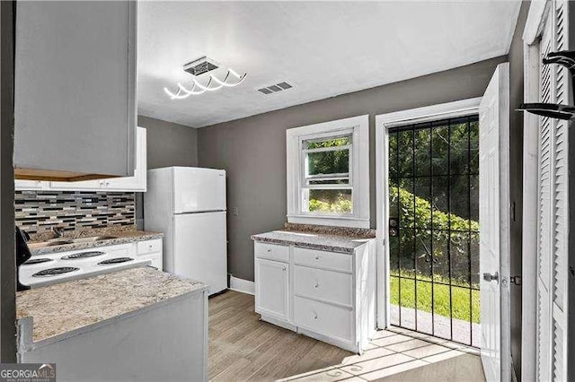 kitchen with white cabinets, white fridge, light wood-type flooring, and backsplash