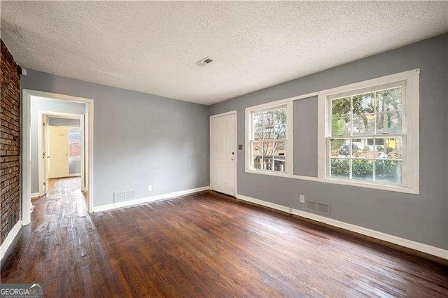 unfurnished room featuring dark hardwood / wood-style floors, a fireplace, a textured ceiling, and brick wall