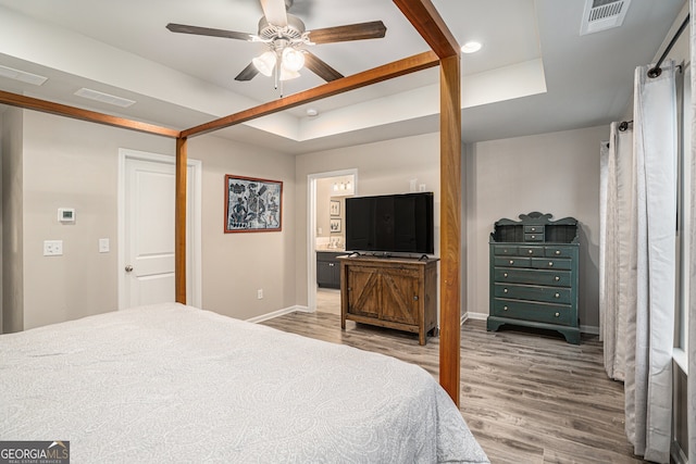 bedroom with a raised ceiling, ceiling fan, ensuite bathroom, and hardwood / wood-style flooring