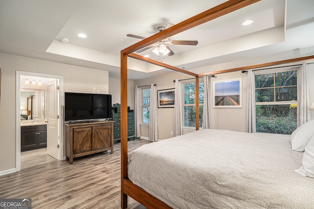 bedroom featuring connected bathroom, light hardwood / wood-style flooring, a raised ceiling, and ceiling fan