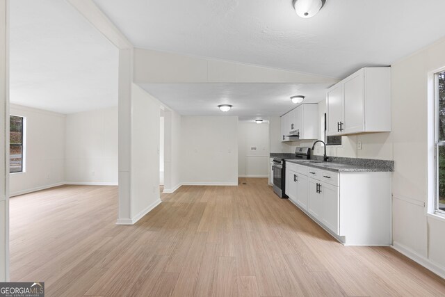 kitchen featuring light wood-type flooring, stainless steel stove, white cabinetry, and lofted ceiling