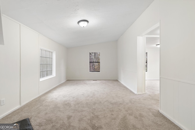 spare room featuring light colored carpet and vaulted ceiling