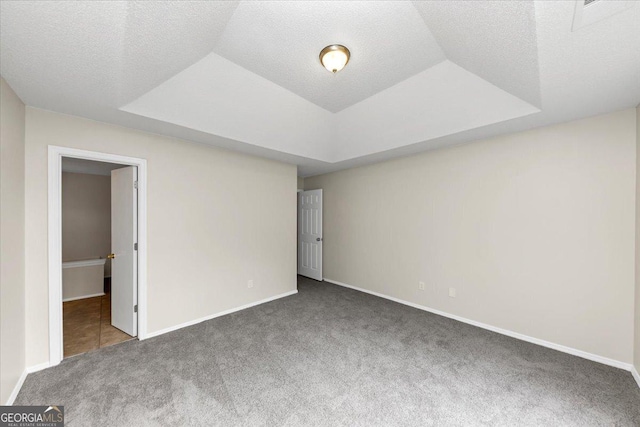 unfurnished bedroom featuring dark carpet, a textured ceiling, and a tray ceiling