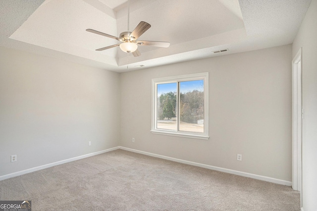 spare room featuring a tray ceiling, light carpet, and ceiling fan