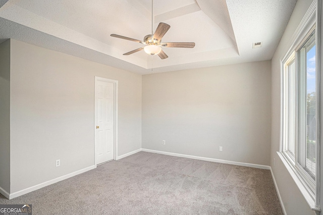 unfurnished room with carpet, a textured ceiling, a tray ceiling, and ceiling fan