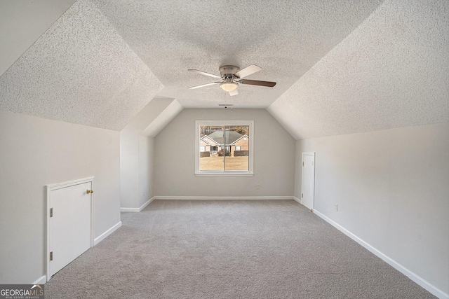 additional living space with a textured ceiling, ceiling fan, light colored carpet, and lofted ceiling