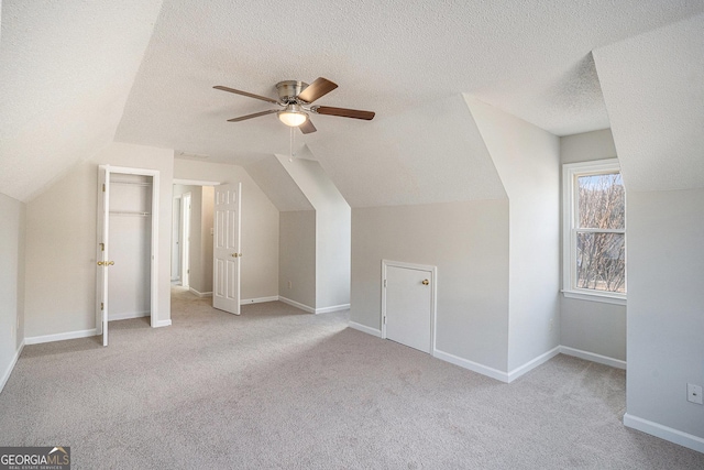 additional living space with lofted ceiling, light carpet, ceiling fan, and a textured ceiling