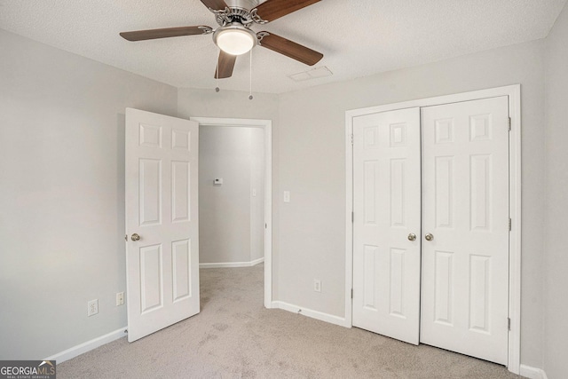 unfurnished bedroom featuring ceiling fan, light colored carpet, a textured ceiling, and a closet