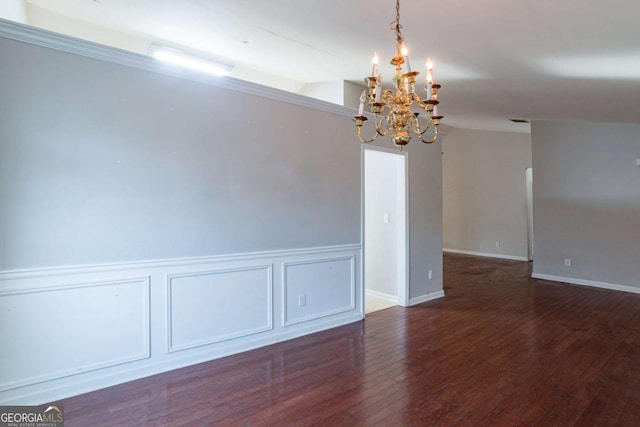 empty room with dark hardwood / wood-style flooring, crown molding, and an inviting chandelier