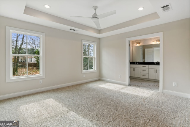 unfurnished bedroom with ensuite bathroom, a raised ceiling, multiple windows, and ceiling fan