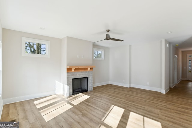 unfurnished living room featuring light wood-type flooring, a wealth of natural light, and a brick fireplace