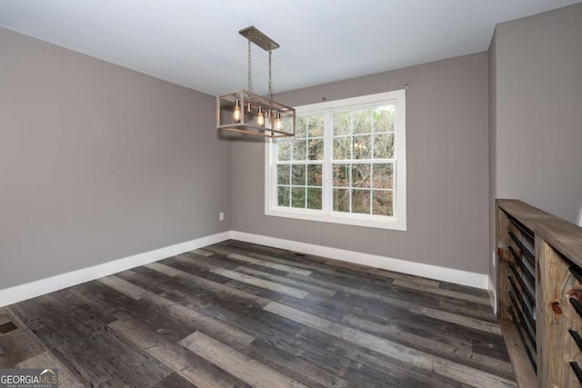 unfurnished dining area featuring a chandelier and dark wood-type flooring