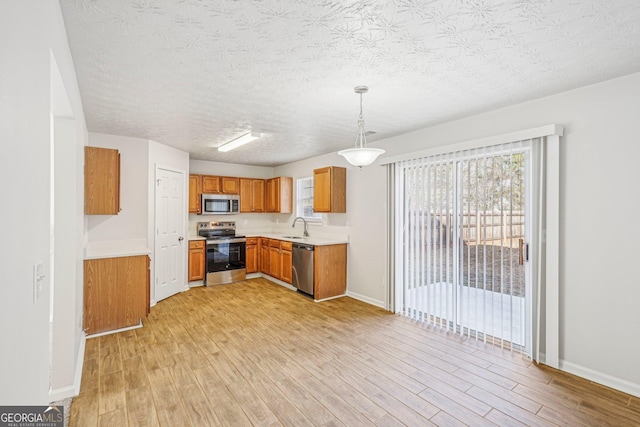 kitchen featuring sink, hanging light fixtures, a textured ceiling, appliances with stainless steel finishes, and light hardwood / wood-style floors