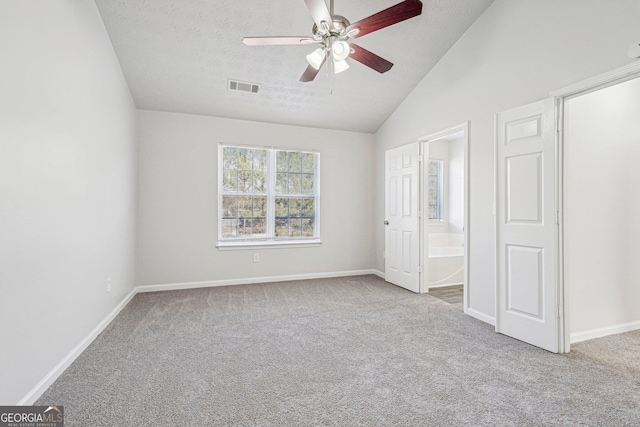 unfurnished bedroom with light carpet, ensuite bath, a textured ceiling, vaulted ceiling, and ceiling fan