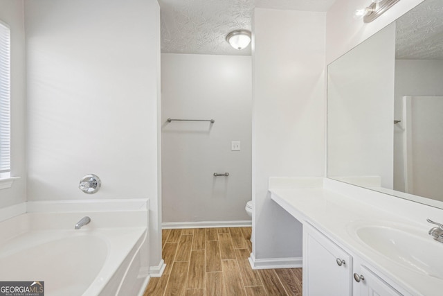 bathroom with hardwood / wood-style floors, vanity, toilet, a textured ceiling, and a tub