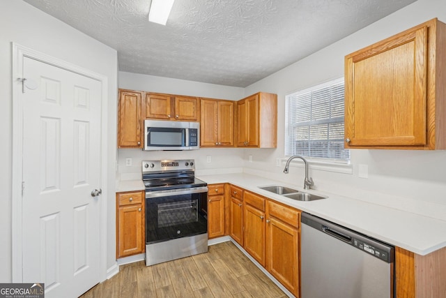 kitchen with a textured ceiling, light wood-type flooring, sink, and appliances with stainless steel finishes