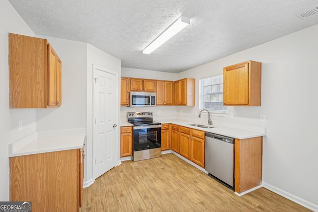 kitchen featuring a textured ceiling, stainless steel appliances, light hardwood / wood-style floors, and sink