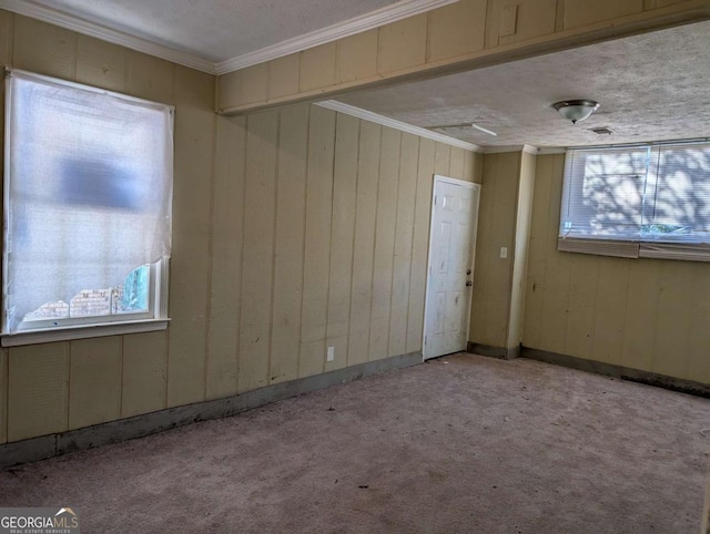 empty room with light carpet, a textured ceiling, crown molding, and wood walls