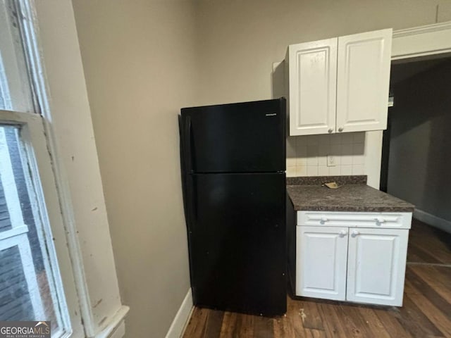 kitchen featuring white cabinets, decorative backsplash, black refrigerator, and dark hardwood / wood-style flooring