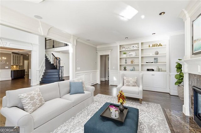 living room featuring ornamental molding, built in features, dark wood-type flooring, and a tiled fireplace