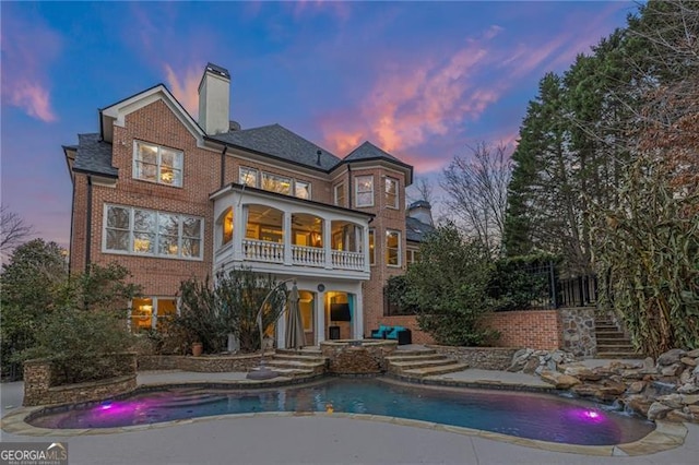 back house at dusk featuring a sunroom and a balcony