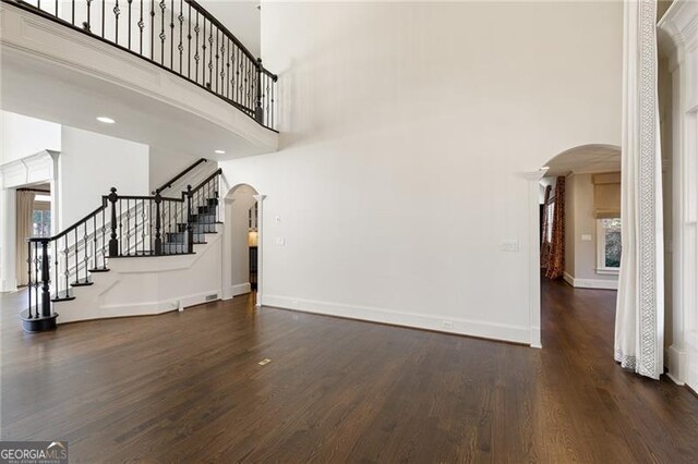 unfurnished living room featuring a towering ceiling and dark wood-type flooring