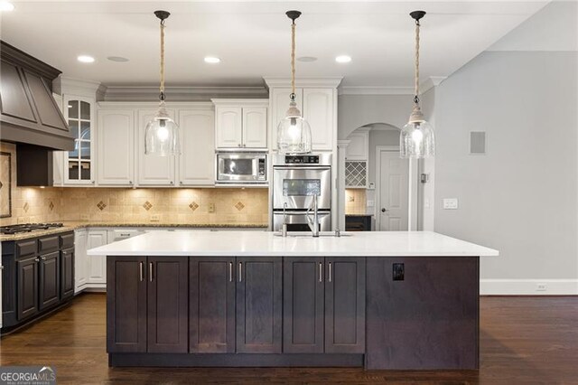 kitchen with pendant lighting, white cabinets, stainless steel appliances, and an island with sink