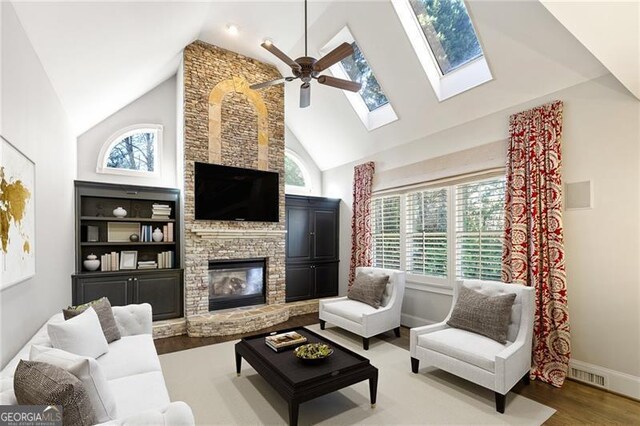 living room featuring a healthy amount of sunlight, a stone fireplace, wood-type flooring, and high vaulted ceiling