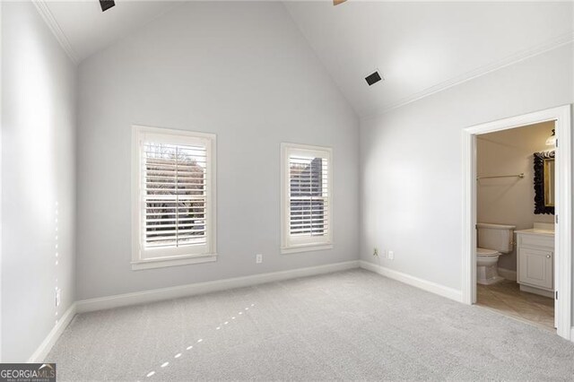 unfurnished bedroom with a walk in closet, ensuite bath, light colored carpet, and high vaulted ceiling