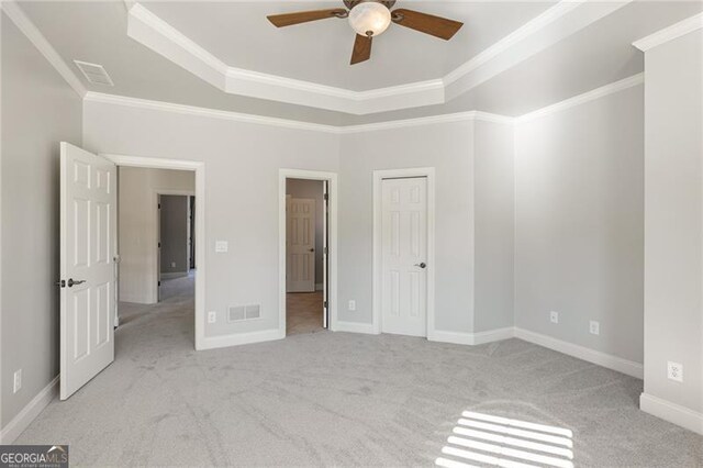 unfurnished bedroom featuring light colored carpet, ceiling fan, ornamental molding, and a tray ceiling