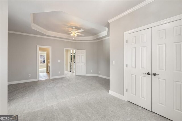 unfurnished bedroom with light colored carpet, a raised ceiling, and ceiling fan