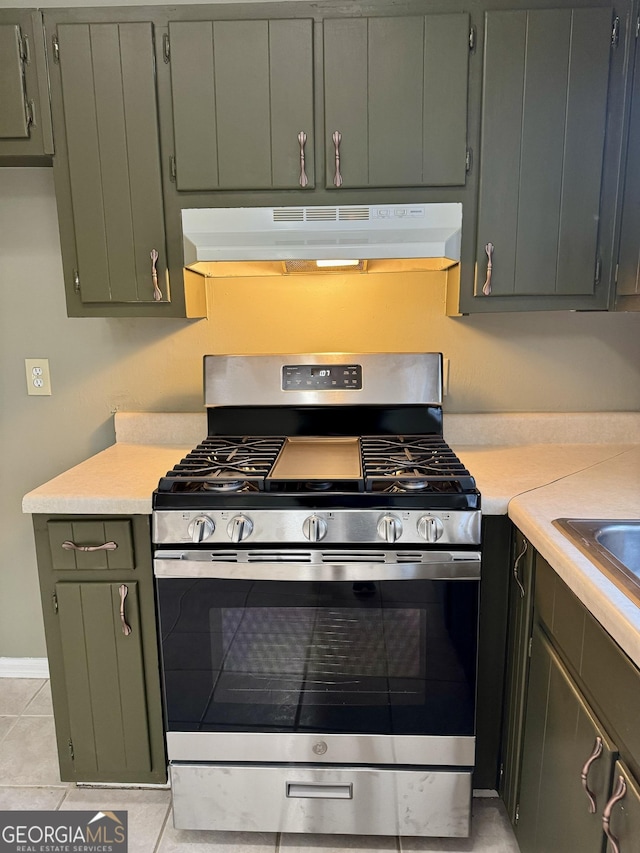 kitchen featuring gas stove, green cabinets, light tile patterned floors, and range hood