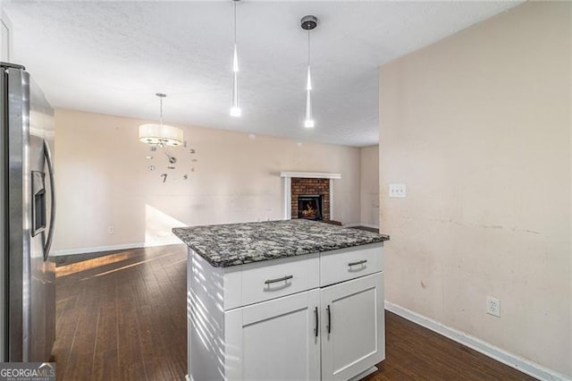 kitchen with dark wood-type flooring, stainless steel fridge, decorative light fixtures, a fireplace, and white cabinets