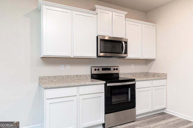 kitchen with light stone counters, white cabinets, stainless steel appliances, and light wood-type flooring