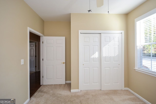 unfurnished bedroom with light carpet, multiple windows, baseboards, and a closet