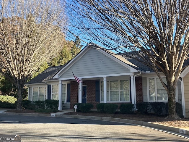 view of front of property with covered porch, brick siding, and a shingled roof